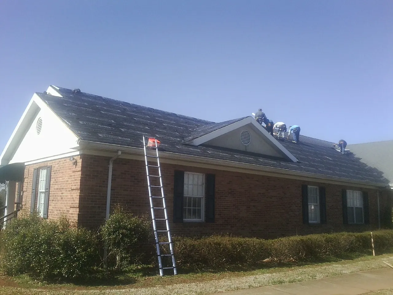 Crew tearing shingles off a brick ranch roof with a ladder set — Emergency Roof Repair work by our crew in Ingomar