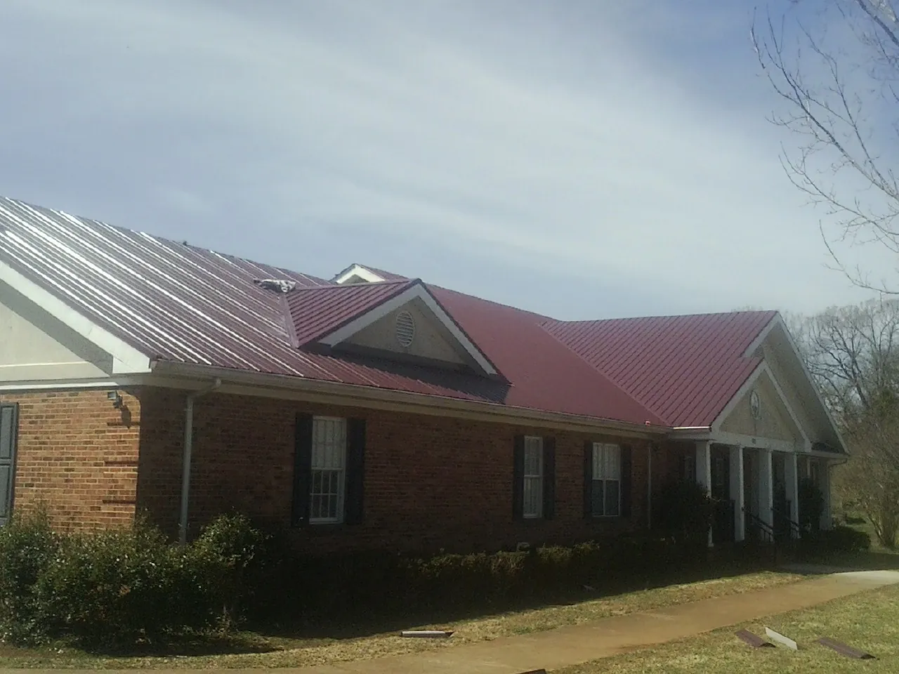 Red metal roof with gabled entries on a long brick building, from a Hail Damage Roof Repair job in Ingomar