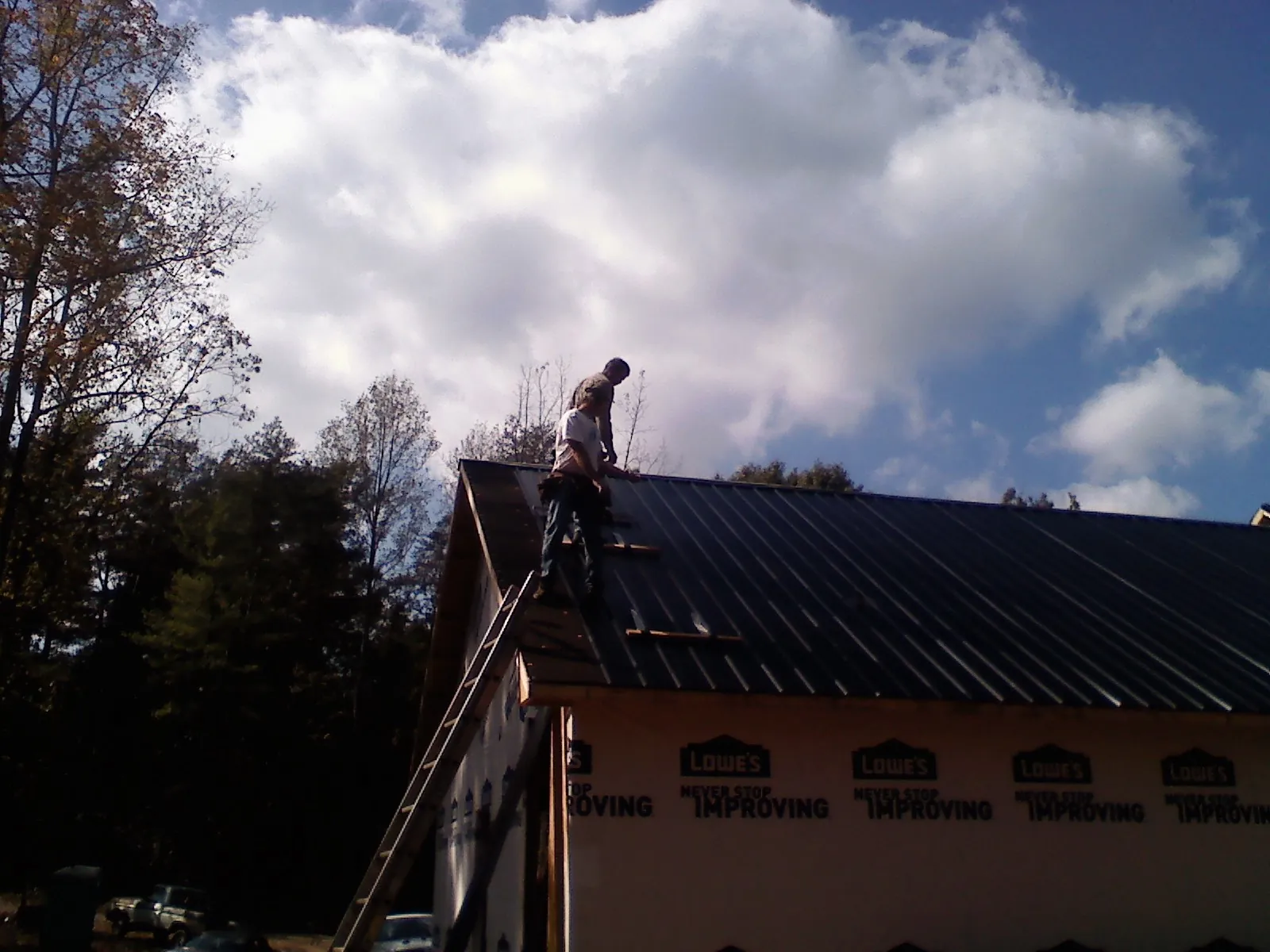 Roofer fastening dark metal panels high against a cloudy sky, from a Roof Inspection job in Ingomar