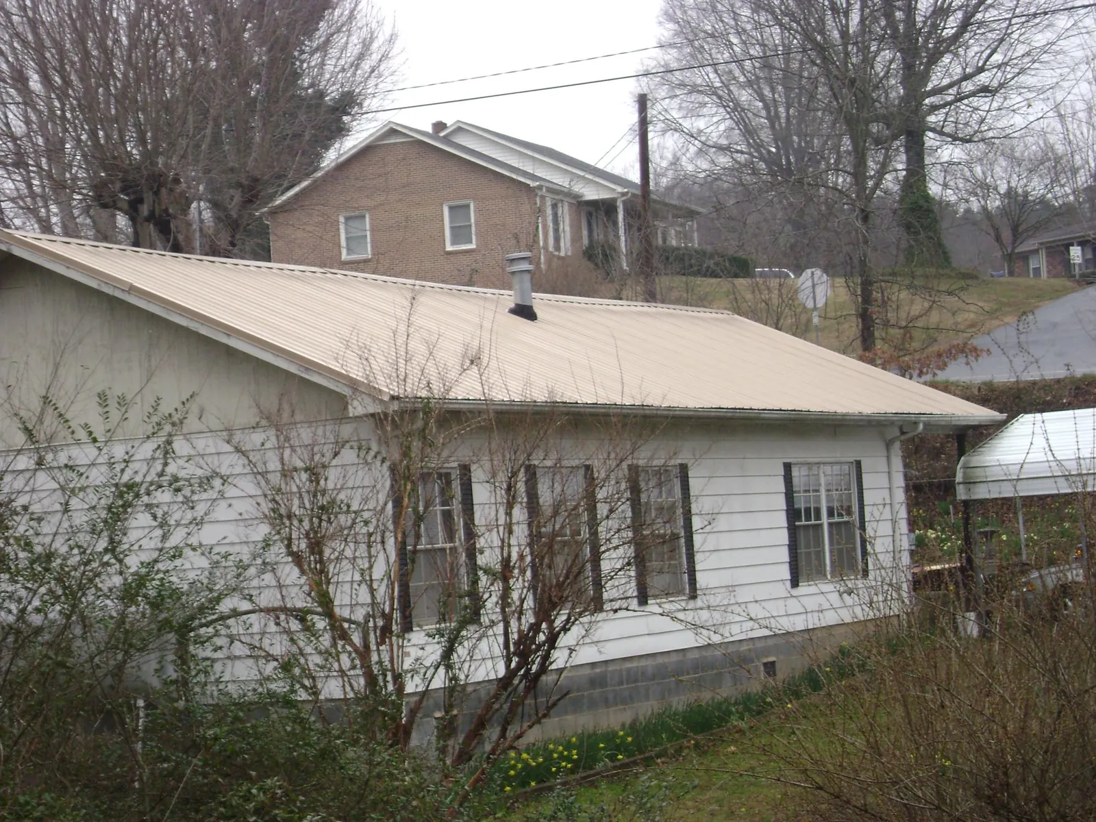 Tan metal roof on a white sided house set into a hillside — Commercial Roofing by Roofing Brothers in Ingomar