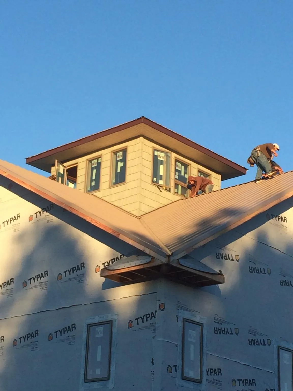 Roofers working around a rooftop cupola on a new metal roof at sunset in Ingomar